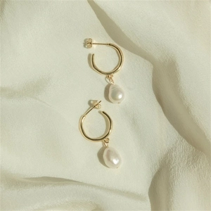 Detailed shot of baroque pearl drop earrings on cream silk fabric with golden hoop rings
