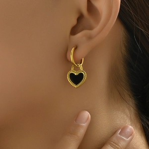 Close-up of a gold hoop earring with a black heart pendant on a model's ear