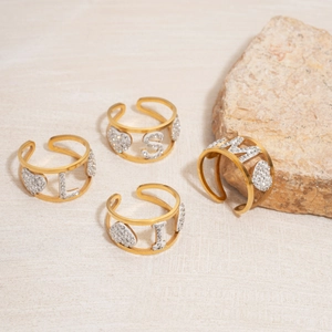 Golden open rings with hollow heart and rhinestone alphabet letters on stone surface