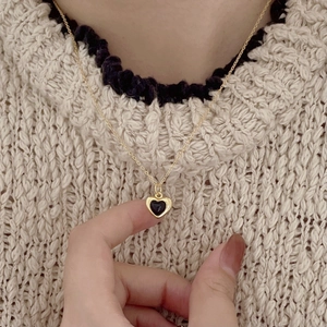 Close-up of heart-shaped black onyx necklace worn on a beige sweater outfit