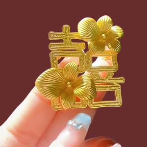 Elegant matte gold double happiness flower brooch held against a solid background