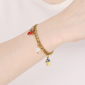 Gros plan d'un bracelet doré avec des breloques cerise, perle et champignon au poignet
