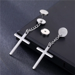 Close-up of silver cross dangle earring with chain and circular stud on dark surface