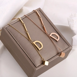Detail of 18K gold titanium necklaces with D letter pendant on a brown jewelry box