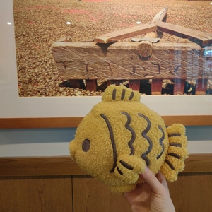 Close-up of curly plush fish-shaped pillow with detailed brown embroidered eyes and scales