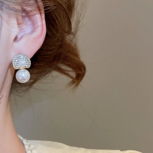 Close-up of elegant gold pearl earring with sparkling rhinestones worn on ear lobe