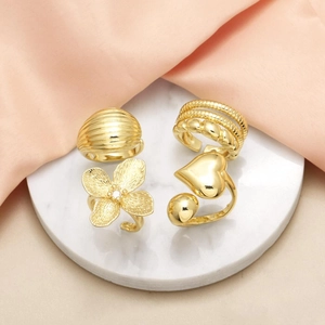 Set of four gold-plated 18k rings featuring heart and flower designs on marble