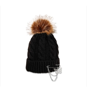 Detailed texture of black cable knit beanie with silver butterfly pin and faux fur pompom
