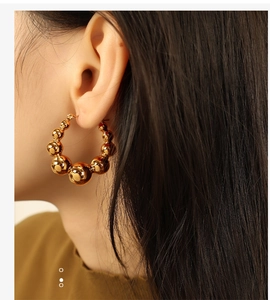 Close-up of a woman wearing gold gradient beaded hoop earrings with a metallic finish