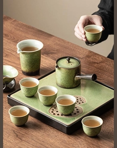 Detailed close-up of a green kiln-fired ceramic tea set including teapot and cups on wood