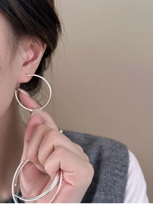 Detailed view of multiple silver circular hoop earrings held in hand by model