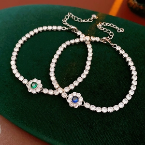 Close-up of zircon flower tennis bracelet with emerald and sapphire accents on green velvet