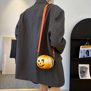 Detail of pumpkin-shaped crossbody bag with smiley face and decorative wide strap on model
