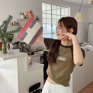 Woman holding a large red, white, and blue woven makeup bag in a modern kitchen setting