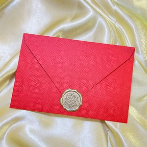 Macro shot of red textured envelope featuring a golden wax seal on yellow silk background