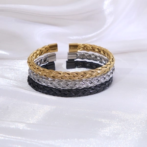 Drei Edelstahl-Armreifen in Gold, Silber und Schwarz auf glänzendem Seidenhintergrund