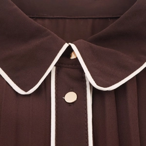 Close-up of dark brown midi dress with white piping and gold buttons on collar