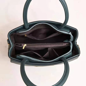 Internal view of dark green tote bag showing multiple compartments and golden zippers