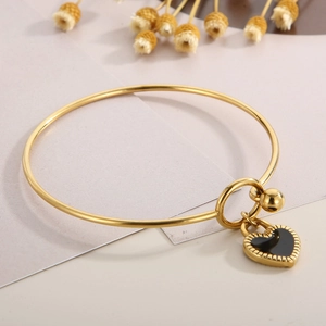 Nahaufnahme eines goldenen Armreifs mit schwarzem Herzanhänger und Blumenhintergrund