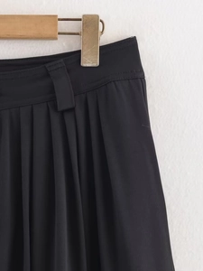 Dettaglio dei pantaloni a pieghe neri a vita alta con trama in twill e passanti per cintura