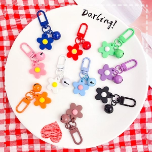 Colorful flower charm bell keychains in 10 vibrant colors on a decorative ceramic plate