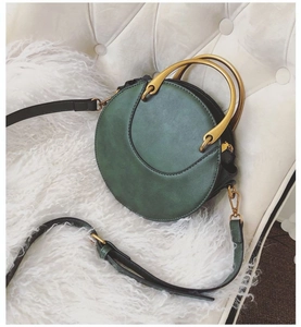 Detail of dark green round crossbody bag with matte finish and gold circular handles