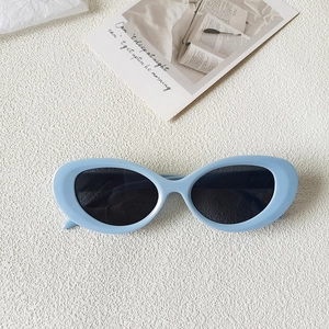 Detail shot of baby blue chunky oval sunglasses with dark lenses on a textured surface