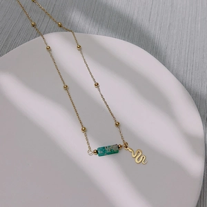 Vintage gold bead necklace with rectangular turquoise and snake charm on white tray