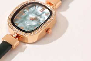 Close-up of rose gold oval watch case with light blue dial and green leather strap
