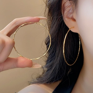 Close-up of large gold chunky hoop earrings with textured finish on a model