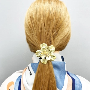 Minimalist golden flower hair tie shown on model hair with intricate alloy petal details