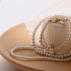 Elegant multi-layer white faux pearl necklace with gold metal clasp on a ceramic plate