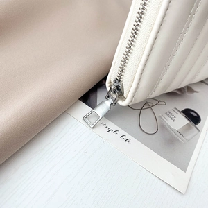 White quilted long wallet for women with silver zipper detail on light wood background