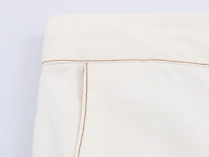 Detailed macro view of white cotton high-waist pants with brown decorative stitching
