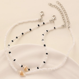 Détail du collier de perles blanches et coquillages posé sur un plateau en céramique