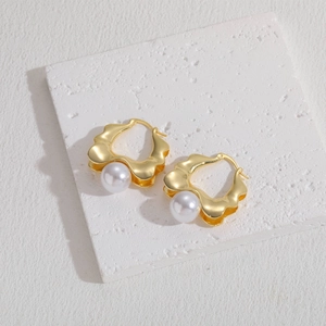 Detail view of gold wavy geometric hoop earrings with pearls on a textured stone surface