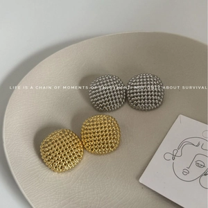 Textured gold and silver hollow sphere stud earrings in a ceramic dish, elegant design