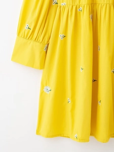 Detailed macro view of yellow dress with white floral embroidery and long sleeve cuffs