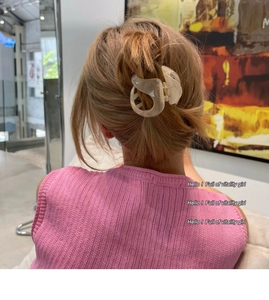 Détail d'une pince à cheveux en résine crème fixant une queue de cheval dans un décor doux