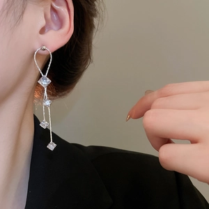 Détail de boucles d'oreilles pendantes argentées avec cristaux de zircon carrés sur modèle
