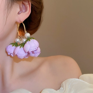 Close-up of a model wearing purple fabric flower and pearl hoop earrings with gold metal