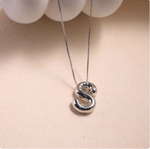 Macro detail of silver balloon style S letter pendant with polished mirror finish surface