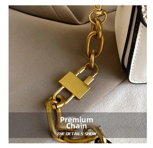 Close-up of golden chain strap and vintage square buckle on white faux leather handbag