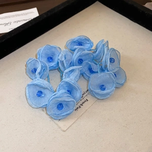 Macro detail of blue organza flower hair tie with faceted beads on beige texture