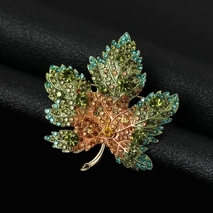 Macro shot of maple leaf brooch with gradient yellow and green rhinestones on gold metal