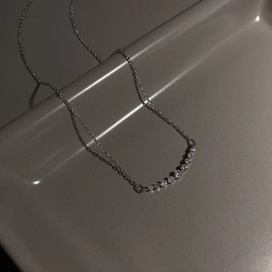Primo piano di un ciondolo a diamante curvo argento su una sottile catena su fondo grigio
