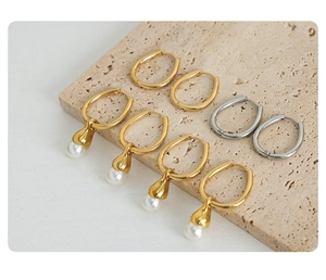 Detail of gold and silver U-shaped hoop earrings with pearls on a beige stone background