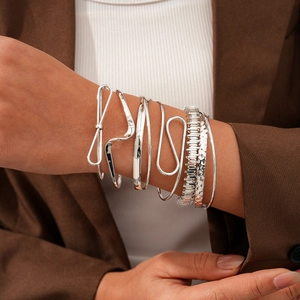 Détail de six bracelets joncs géométriques torsadés argentés portés par un mannequin