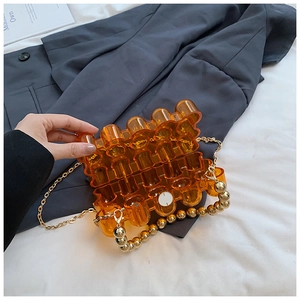 Detail of amber acrylic modular handbag with gold bead handle and metallic chain strap