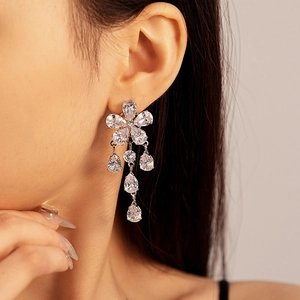 Macro shot of silver flower earrings featuring zircon tassel pendants on a female model